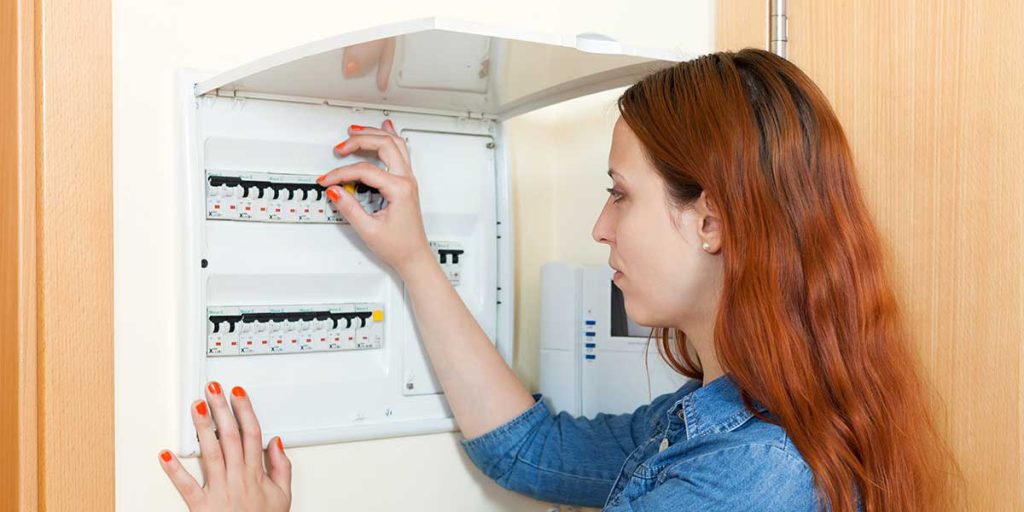 A woman inspecting and switching circuit breakers on a home electrical panel to prepare her electrical system for hurricane season.